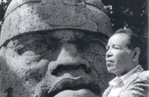 Fotografía histórica en blanco y negro de Armando Lavalle junto a una escultura monumental de rasgos prehispánicos.