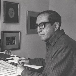 Fotografía en blanco y negro de Joaquín Gutiérrez Heras trabajando con una partitura en su escritorio.